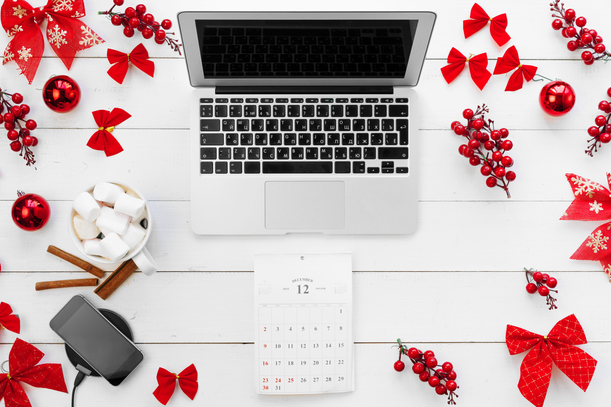 Laptop on white wooden desk surrounded with red Christmas decorations, top view