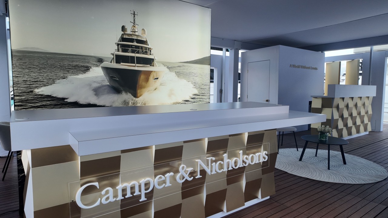 Camper & Nicholsons trade show booth at the Fort Lauderdale Boat Show, featuring a sleek backlit tension fabric display showcasing a luxurious yacht on calm waters.